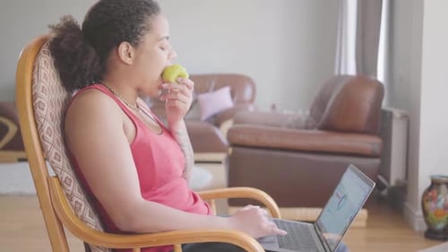 Woman Using Laptop, Eating Apple Indoors