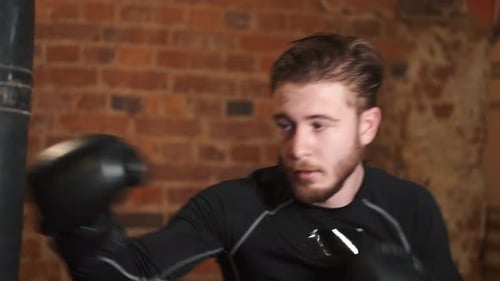 Dedicated Young Man Punching Boxing Bag at Gym