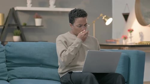 Person Coughing While Using Laptop on Sofa
