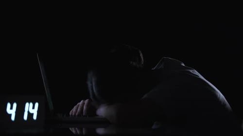 Dark Haired Person Slumped over Laptop at Night