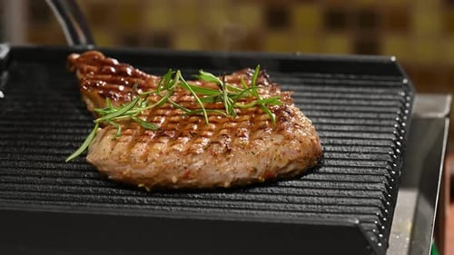 grilled piece of pork with a bone is on the grill and sprinkled with green rosemary