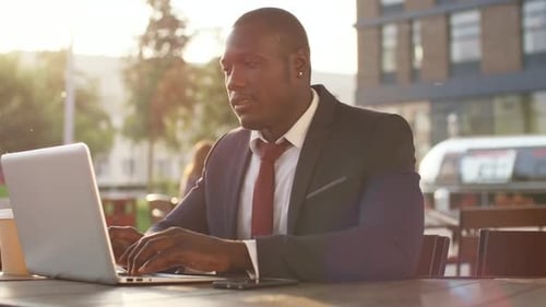 Man in Suit Works on Laptop at Outdoor Table