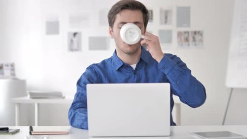 Lässiger erwachsener Mann trinkt Kaffee beim Arbeiten am Laptop