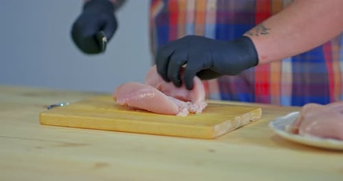 Homem corta carne de frango crua em uma tábua de madeira