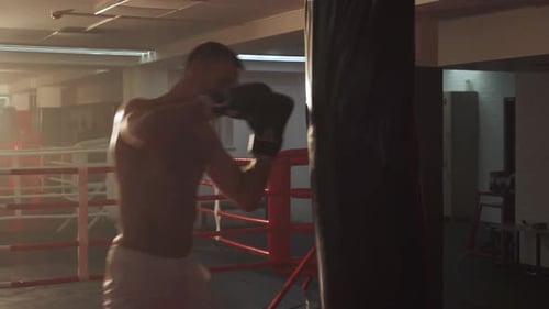 Aggressiver Mannkämpfer trainiert seine Schläge, schlägt einen Boxsack, Trainingstag im Boxstudio