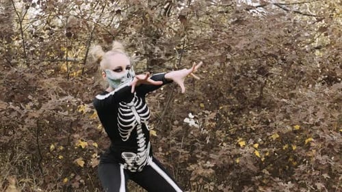 A girl with a scary make-up in a skeleton costume, a mask with rhinestones in a gloomy autumn forest