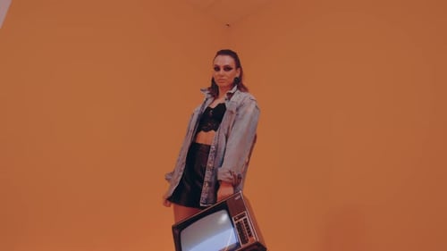 Stylish Woman Holding Analog Television in Orange Room