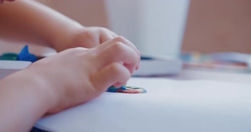 A Little Boy Plays with Bright Clay or Plasticine, Sitting at the Table