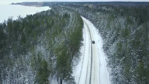 Flying Above Car Driving on a Winding Road Passing Through the Snowy Winter Forest