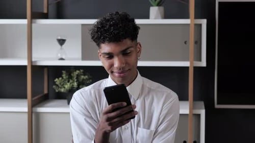 Young Adult Uses Smartphone, Smiling Indoors