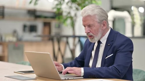 Frustrated Senior Man at Workplace Using Laptop