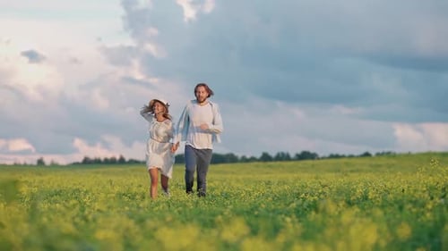Countryside Cheerful Young Couple in Nature Man and a Woman are Running Through a Field of Rapeseed