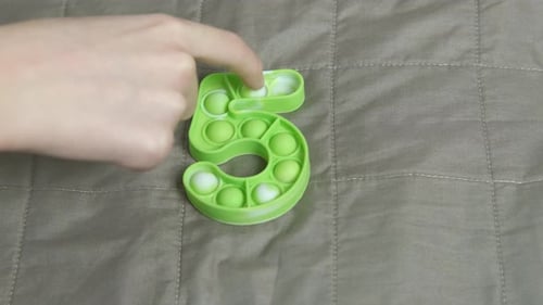 Child Playing With Light Green Number Five Pop-It Toy