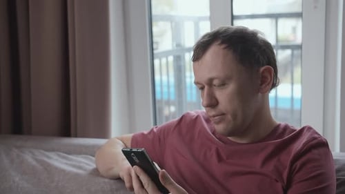 Man Relaxing on Couch Uses Smartphone