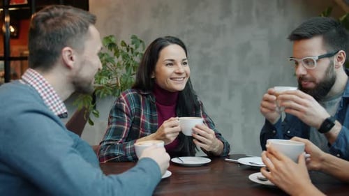 Joyful Friends Male and Female Talking and Drinking Coffee at Table in Cafe
