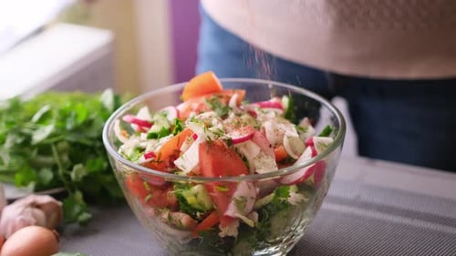 Woman Adding Salt and Spices Into Mixed Salad of Vegetables Tomatoes Cucumbers Onion Parsley