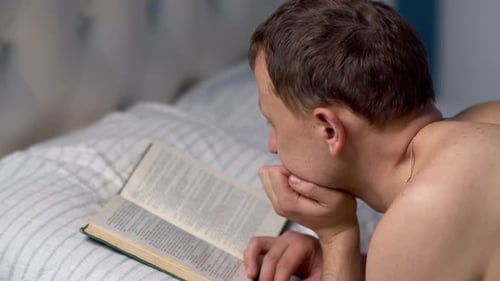 Man reading a book before going to bed, lying in bed