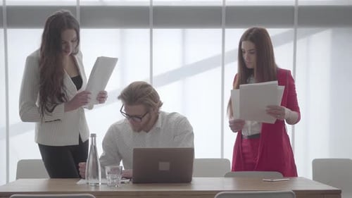 Blond Man in Glasses Sitting in a Light Comfortable Office with Netbook at the Table Signing