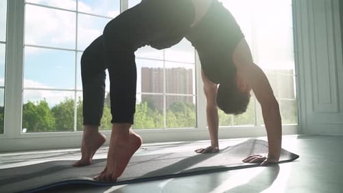 Wellness, Man Doing Yoga in a White Room Filled with Light, Man Performs the Bridge Pose Near the