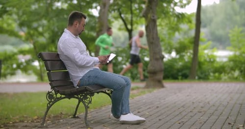 Man Using Tablet on Park Bench in Daytime