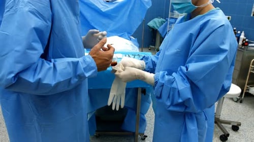Krankenschwester hilft einem Chirurgen beim Tragen von OP-Handschuhen
