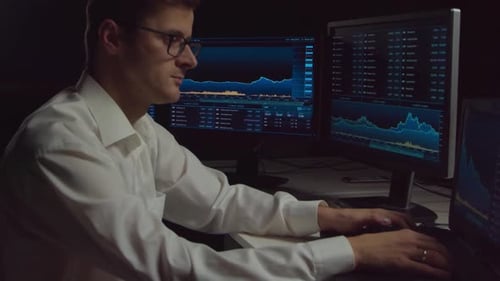 Händler, der nachts im Büro arbeitet und Workstation- und Analysetechnologie verwendet.