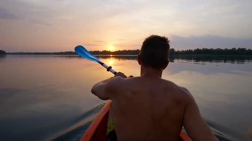 A Man Kayaks on a Calm River Towards the Sunset