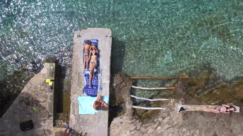 Two women and a girl sunbathing on dock