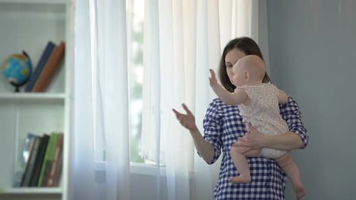 Mother Holding Baby Pointing at Window at Home