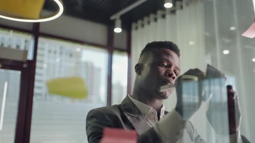 Homme d'affaires afro-américain utilisant des notes autocollantes remue-méninges stratégie de résolution de problèmes sur verre