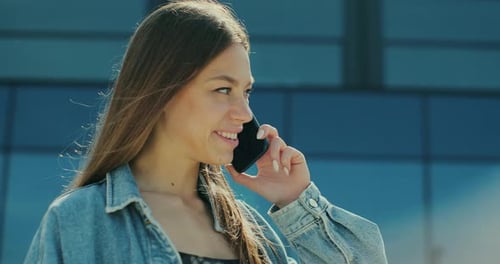 Junge Frau lächelt selbstbewusst und spricht auf der Straße mit dem Smartphone