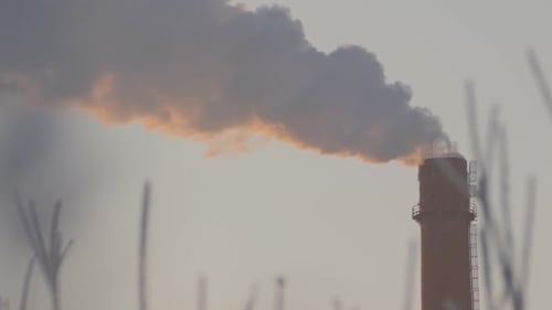 Über eine Nahaufnahme des Schornsteins einer Fabrik oder Fabrik, die großen Rauch in den Himmel bläst. Der Rauch