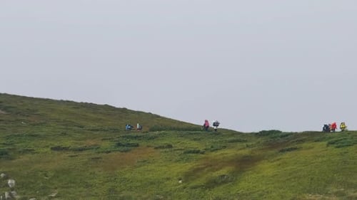 Group of Tourists with Hiking Backpacks Climbs the Mountain Range. Afar View