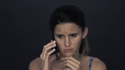 Distraught Woman Talking on Cellphone Against Dark Background