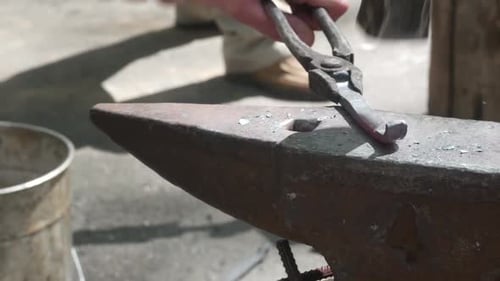 Metal Worker Using Hammer and Tongs on Anvil