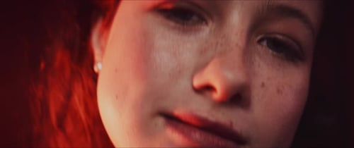 Close up of a ginger curly girl face while dancing and moving in red neon lights
