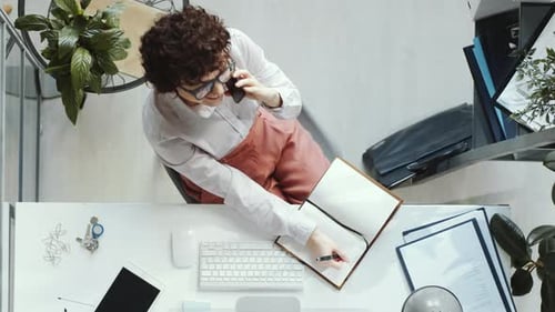 Top Down of Business Lady Talking on Phone and Taking Notes in Office