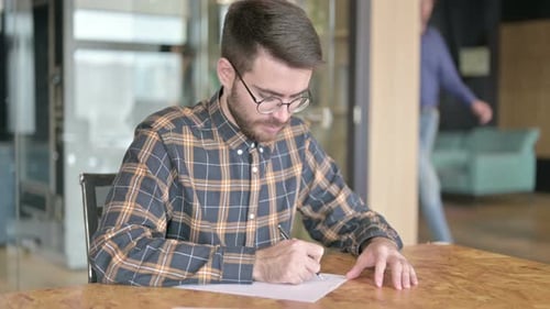 Focused Young Designer Writing on Paper in Office