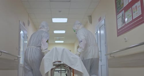 Doctors in Protective Suits Carry the Patient on a Stretcher Along the Corridor of the Clinic
