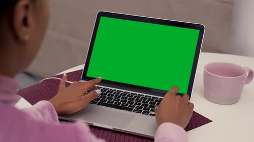 Over the Shoulder Shot of a Black Woman Sitting at the Table and Typing on Laptop with Green Chroma