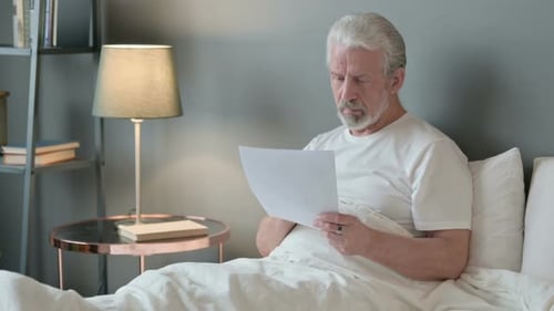 Senior Adult Reading Papers in Bed