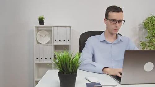 Young and Handsome Office Worker Sitting at His Desk Works on a Laptop