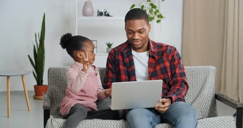 Young Adult and Child Use Laptop on Couch