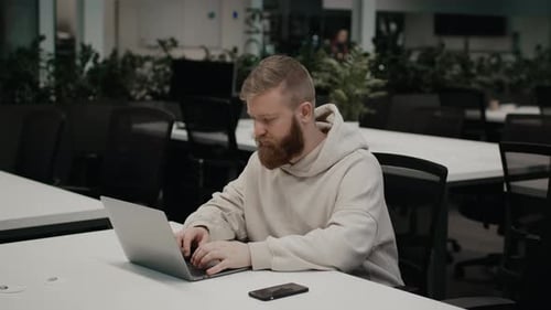 Cara barbudo usando laptop no local de trabalho sentado na mesa interna