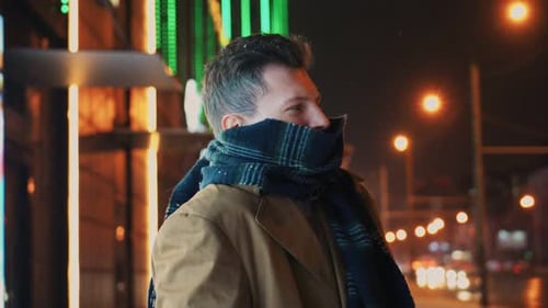 Man Freezing From Cold Standing Near Roadway and Shopping Center at Night