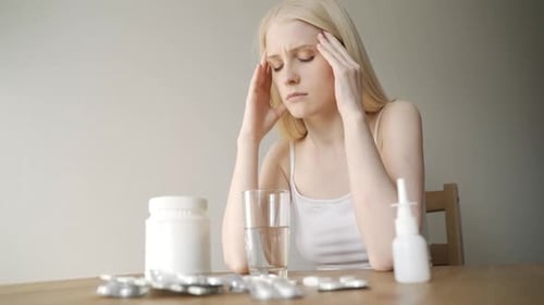 Joven enferma y triste se sienta a la mesa con diferentes medicamentos