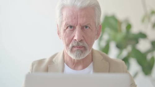 Close Up of Old Man Looking at Camera While Using Laptop in Office