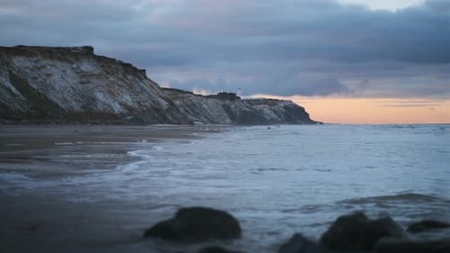 Sea Over Sandy Beach With Dramatic Cliffs At Sunset
