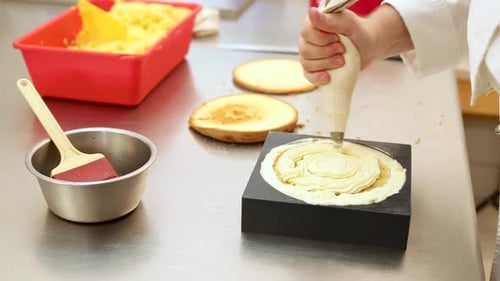 Pastry chef at work in a restaurant kitchen decorating a sweet cake with whipped cream