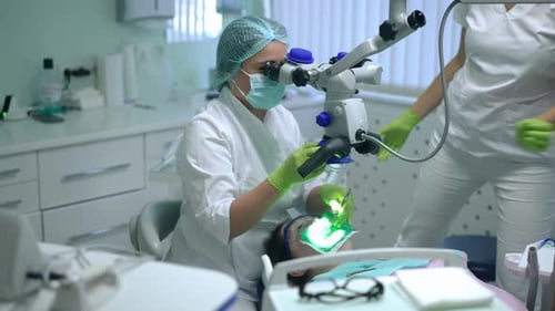 Konzentrierter Zahnarzt untersucht mit einem Dental-Mikroskop die Mundhöhle des Patienten als Assistentin